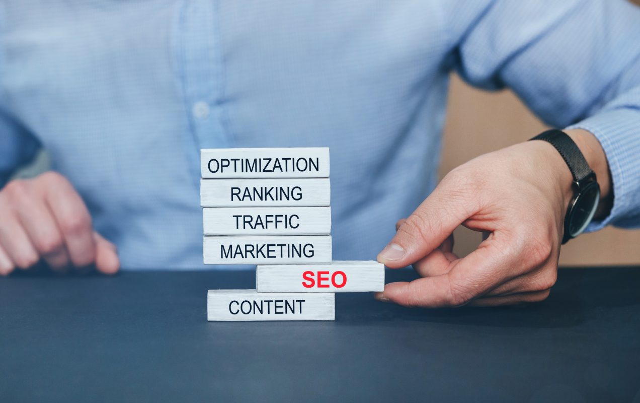Hand stacking wooden blocks labelled Optimization, Ranking, Traffic, Marketing, SEO and Content